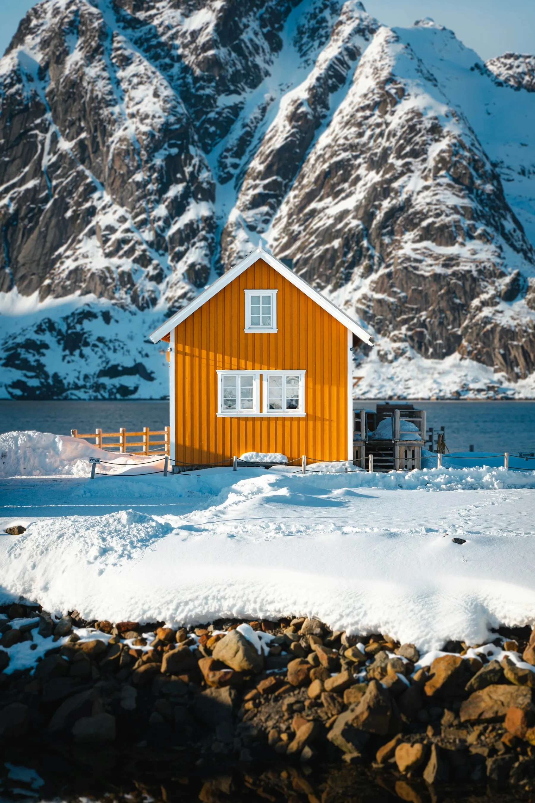 A bright orange wooden house in a snowy landscape below mountains